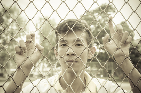 asian young man caged behind metal or steel netの写真素材