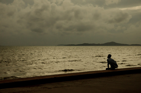 Silhouette guy sitting on breakwater in evening near seaの写真素材