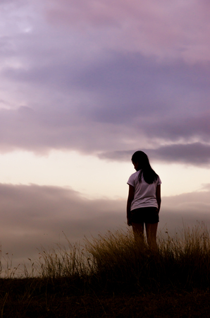 woman standing alone at the field during beautiful sunsetの写真素材