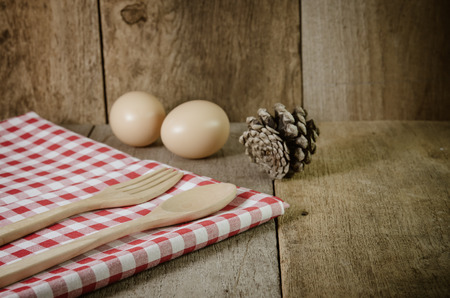 Tablecloth, wooden spoon, fork and eggs on wood textured backgroundの写真素材