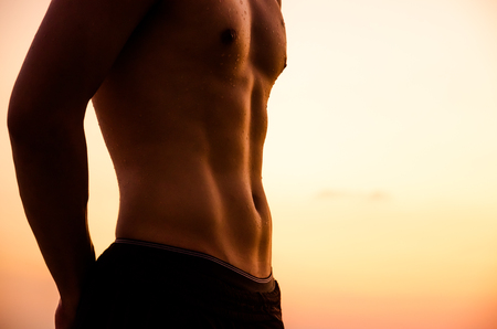 Torso of strong man against sunset beach background