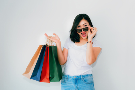 Woman wears white t-shirt and jean is holding many shopping bags in front of bright white background with surprise emotion.の写真素材