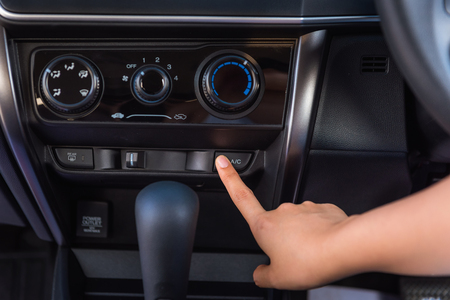 Close up of woman hand pressing turn on air-conditioner button a car.の写真素材