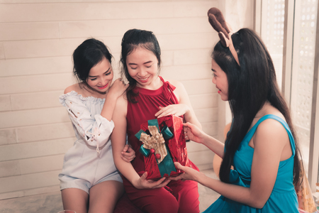 Portrait of an asian girls giving surprise gift to her friends in house party.の写真素材