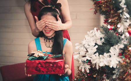 Portrait of an asian girls giving surprise gift to her friends in house party.の写真素材