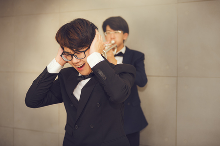 Young man playing trumpet instrument to noisy behind of his friend in musical room., Teens musician orchestra having irritated his friend while he playing trumpet., Noisy hazard pollution.の写真素材