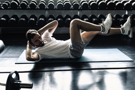 Portrait of sporty man exercising in fitness gym., Athletic young man doing sit-ups or cycling workout posing in front of dumbbells row background., Wellness and healthcare concept.の写真素材