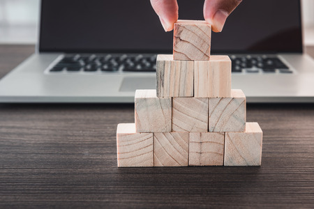 Closeup finger man is pick up wooden cube from stack in front of computer laptop., Business and technology concept.の写真素材