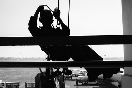 Worker is cleaning windows glass in the airport terminal., Silhouette of employee is rappelling for wipe cleaning exterior glass of building., Occupation and service concept.の写真素材