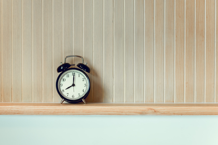 Vintage Retro of Alarm Clock on Headboard Shelf, Interior Bedroom and Decorative Design. Black Timer Clock is Layout Against on Isolate Stripes of Wooden Background.の写真素材