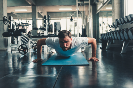Sporty Man is Push-Up Exercising in Fitness Gym., Portrait of Young Handsome Man is Working Out Against on Sport Bodybuilding Equipment Background., Healthcare and Leisure Activities Concept.の写真素材