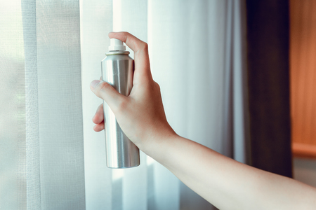 Woman Hand is Spraying Air Freshener to Curtains Window in Bedroom, Unpleasant smell and Aromatherapy Concept.の写真素材