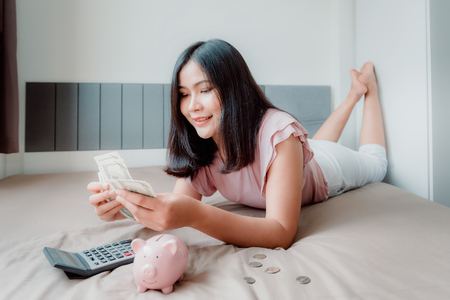 Portrait of Beautiful Woman is Calculating Money Saving While lying on Her Bedroom. Business Financial and Investment Concept.の写真素材