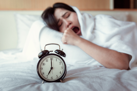 Turning off Sound or Snoozing The Alarm Clock Concept, Beautiful Woman Waking Up in The Morning at Bedroom While Her Hand is extending Alarm of Timer Clock.の写真素材