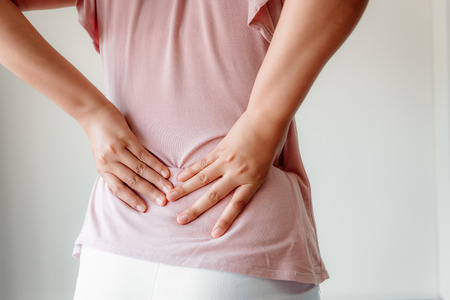 Close-Up of Woman Hands is Massaging Her Waist on Isolated Gray Background, Young Adult having Backache After Home Work. Healthcare and Medicine Concept.の写真素材