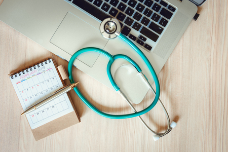 Business Healthcare Medicine and Insurance Concept.Top View of Stethoscope on a Laptop With Calendar Checkup Concept., Annual Doctor Appointment for Physical Check-Up Against Wooden Background.の写真素材