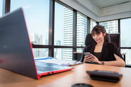 Portrait of Business Woman is Using Mobile Phone in Office Workplace, Attractive Beautiful Businesswoman is Chatting Message on Cellphone While Working at Her Workspace., Communication Concept.の写真素材