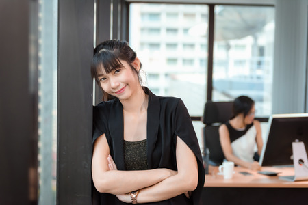 Portrait of Beautiful Attractive Business Woman Standing Beside Windows Frame in Modern Office, Confident Asian Girl in Arms Crossed Posing While Looking at Camera. Occupation and Financial Conceptの写真素材