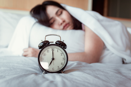 Pretty Young Woman is Sleeping and Alarm Clock in Bedroom, Beautiful Girl is Sleeping on Her Bed and Relaxing in The Morning., Healthcare and Lifestyles Concept.の写真素材