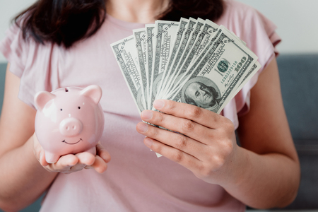 Close-Up Woman Hands is Holding Money Cash and Piggy Bank in Her Bedroom, Pink Piggy Saving, Business Banking and Financial Concept.の写真素材