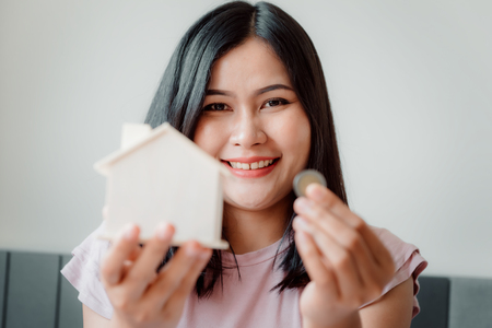 Close-Up of Woman is Showing Money Coin and Housing Bank on The Bedroom., Female Hand is Inserting Coin in House Saving. Business Banking and Financial Concept.の写真素材