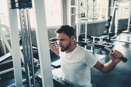 Handsome Man is Exercising With Lifting Machine in Fitness Club, Portrait of Strong Man Doing Working Out Calories Burning in Gym, Healthy and Fitness Lifestyle Concept.の写真素材