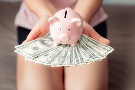 Woman Hands is Holding Piggy Bank and Dollar Money Cash on Her Bedroom, Business Banking or Financial Concept.の写真素材