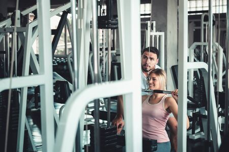 Beautiful Woman is Exercised Training With Bodybuilder Machine in Fitness Club., Attractive of Sporty Girl Doing Working Out With Her Trainer in Gym, Healthy and Sport Exercising Lifestyle Concept.の写真素材