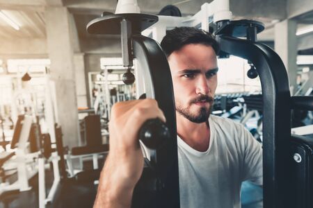 Handsome Man is Exercising With Bodybuilder Machine in Fitness Club.,Portrait of Strong Sporty Man Doing Working Out Calories Burning in Gym., Healthy and Fitness Sport Lifestyle Concept.の写真素材