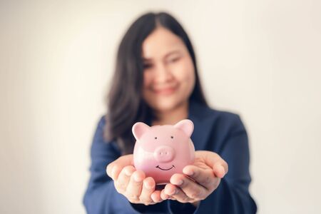 Business Woman Investor Holding Piggy Bank for Money Savings on Her Hands, Asian Businesswoman in Uniform Suit Showing Money Saving While Looking at Camera., Investment and Financial Concept.の写真素材