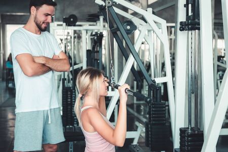 Portrait of Beautiful Woman is Exercised Training With Bodybuilder Machine in Fitness Club., Attractive of Sporty Girl Doing Working Out With Her Trainer in Gym, Healthy and Sport Lifestyle Concept.の写真素材