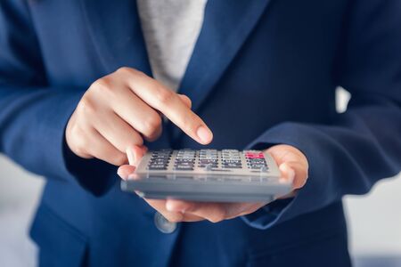Close-Up of Business Accountant Financial Using Calculator for Estimated Tax Earning Account, Entrepreneurs Woman in Uniform Suit is Calculating Investment Income Tax. Business Finance and Investing.の写真素材