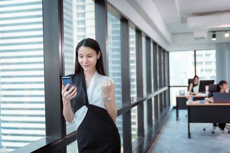 Business Woman Having Excited and Happy After Project Dealing Successful While Using Smartphone., Businesswoman Exciting and Celebrate Success With Rise Hand Up While Holding Her Cell Phone.の写真素材