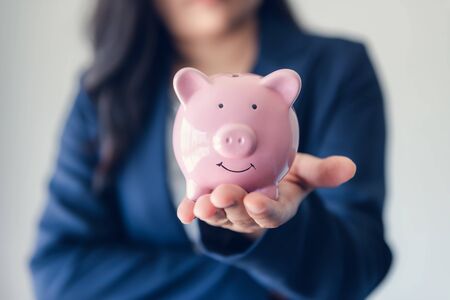 Business Woman Investor Holding Piggy Bank for Money Savings on Her Hands, Asian Businesswoman in Uniform Suit Showing Money Saving While Looking at Camera., Investment and Financial Concept.の写真素材