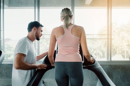 Beautiful Woman is Exercise Training With Treadmill Machine in Fitness Club., Attractive of Sporty Girl Doing Working Out With Her Trainer in Gym, Healthy and Sport Exercising Lifestyle Concept.の写真素材
