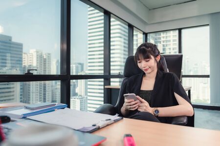 Business Woman Finance Accountant Using Mobile Phone for Chat Communicating While Working With Computer in Her Office Desktop, Business Financial Accounting and Technology Communication Concept.の写真素材