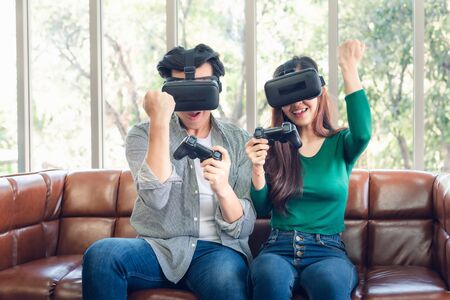 Young Couple Having Fun While Playing Virtual Reality Game Together in Their Home. Couple Love Having Enjoyment With Electronic VR Goggles Gaming on Couch. Entertainment Innovation/Lifestyles Conceptの写真素材