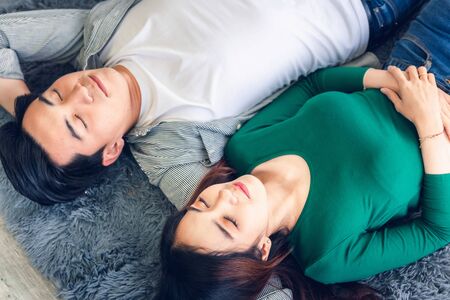 Young Couple Having Relaxing While Lying on Carpet at Their Home, Attractive Asian Couple Love are Relaxed Together on Living Room Flooring. Happy Moments and Lifestyles Conceptの写真素材