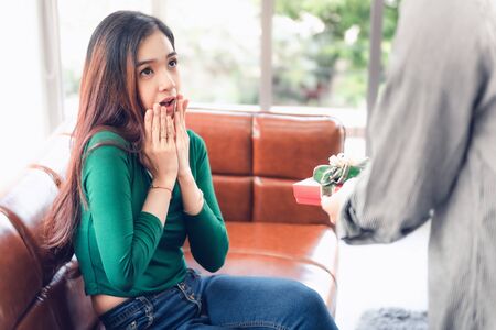 Romantic Surprise and Couple Love Valentine Concept, Young Man is Presenting Surprised to His Girlfriend at Home. Beautiful Woman Having Happiness and Surprise While Her Boyfriend Giving Presents Box.の写真素材