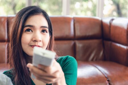 Close-Up of Asian Woman is Turn-On/OFF Air Conditioner Split Type by Remote Controller in Living...