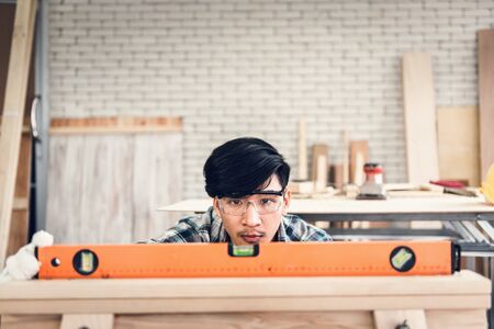 Carpenter Man is Working Timber Woodworking in Carpentry Shop, Craftsman is Leveling Alignment Timber Plank for Wooden Furniture in Workshop. Workmanship and Job Occupation Conceptの写真素材