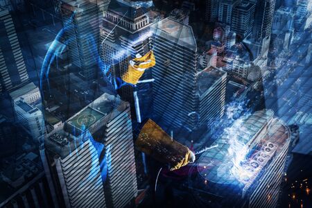 Double Exposure of Welder is Welding Pipeline Fabrication Assembly on Cityscape Urban Downtown Background. Technician Welding in Safety Protective Equipment is Working Metalwork.の写真素材