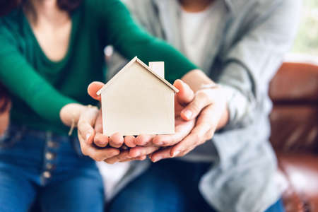 Couple Hands Holding Housing Model for Future Real Estate Saving, People Hand Joint to Protection Home Property Togetherness. House Insurance and Residential Loan Investment Concept.の写真素材