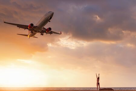 Travel Destination and Vacation in Summer, Sexy Woman Having Fun While Capturing Photos Airplane is Flying Over The Beach. Tourist Woman Relaxing on Tropical Beach and Enjoy Seeing Landing Aircraft.の写真素材