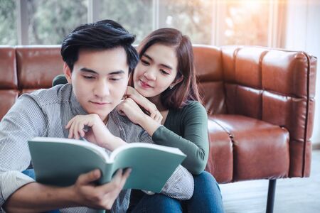 Portrait of Young Couple Love in Romantic Emotions While Reading a Book Together, Couple Young People Having Fun and Relaxing in Living Room. Happy Emotion and Relaxation Lifestyles Conceptの写真素材