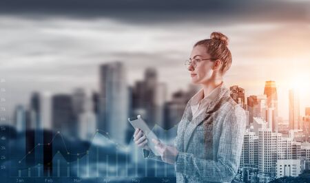 Double Exposure of Attractive Business Woman Woking on Tablet on Cityscape Background With Infographics Chart, Businesswoman Leader Management Standing on City Urban and Business Media Market Screen.の写真素材