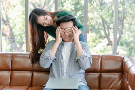 Romantic Couple Love and Valentine Celebration Concept, Young Woman is Presenting Gift to Her Beloved Boyfriend in Living Room. Couple Lover Giving Present Gift Box Together in Celebrating Birthdayの写真素材