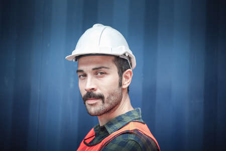 Portrait of Confident Transport Engineer Man in Safety Equipment Standing in Container Ship Yard. Transportation Engineering Management and Containers Logistics Industry, Shipping Worker Occupationの写真素材