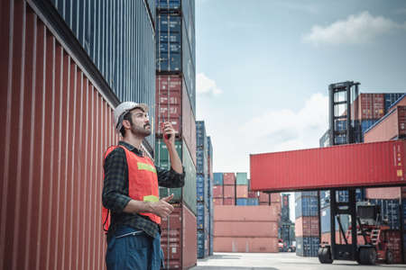 Container Logistics Shipping Management of Transportation Industry, Transport Engineer Managing Control Via Walkie Talkie in Containers Shipyard. Business Cargo Ship Import/Export Factory Logistic.の写真素材