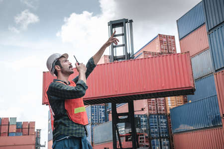 Transport Container Engineer Managing Control Via Walkie Talkie in Containers Shipyard. Container Logistics Shipping Management of Transportation Industry, Business Cargo Ship Import/Export Factoryの写真素材